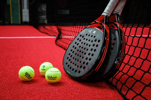 Padel Bälle auf einem roten Court und 2 Schläger am Netzt angelehnt